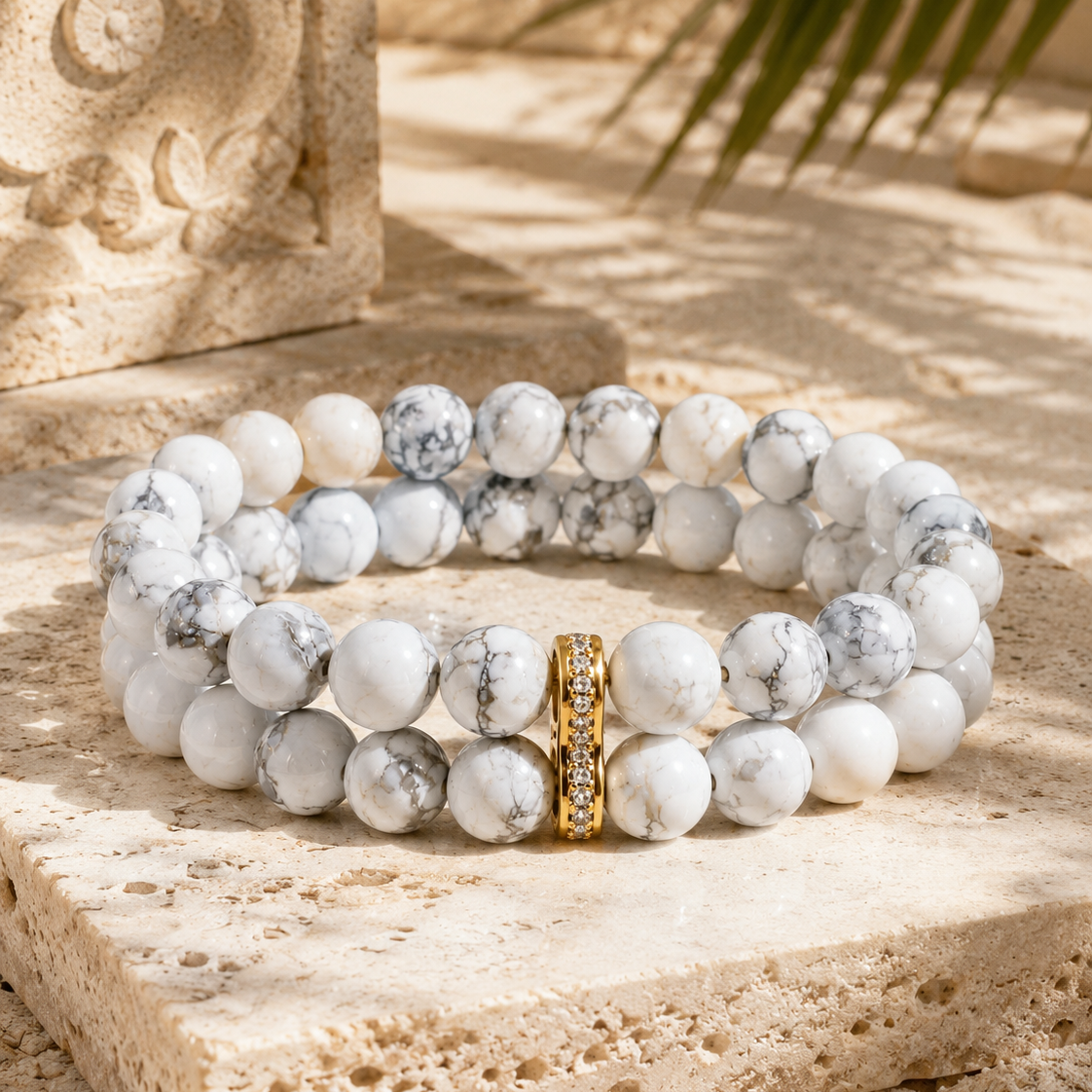 Bracelet MAÏA en howlite blanche double rang posé sur travertin, lumière chaude et ombres de feuilles