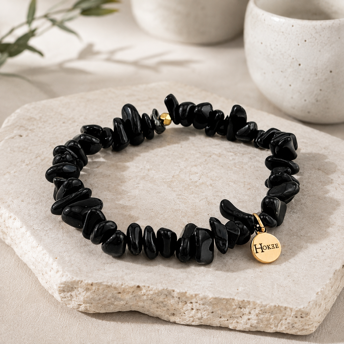 Bracelet puce en obsidienne noire naturelle posé sur un support minéral avec médaillon doré HOKEE